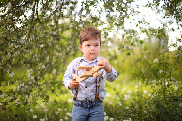 Little cute blond boy playing with a wooden plane in the summer park on the grass on a sunny day, focus on the child