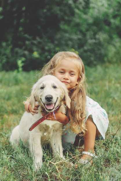 Little cute blond girl playing with her puppy golden retriever in summer in the park.