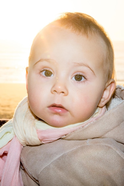 Little cute blonde child girl looking right at camera with sunset