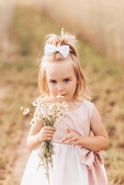 Piccola ragazza bionda carina con un mazzo di fiori di campo in natura in estate