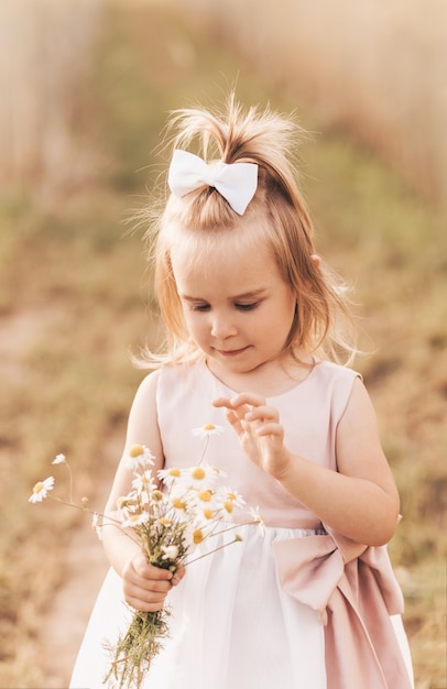 Piccola ragazza bionda carina con un mazzo di fiori di campo in natura in estate