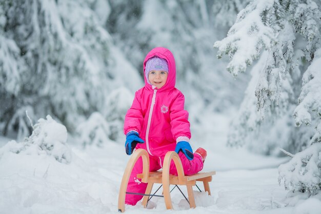 Маленькая милая голубоглазая девочка катается на санках в заснеженном лесу. зимний сад. деревья в снегу.