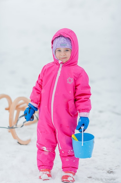 Little cute blue-eyed girl sledding in a snowy forest. Winter Garden. Trees in the snow.