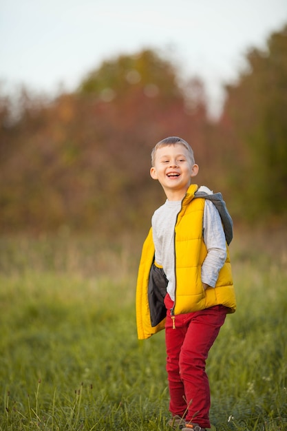 Маленький милый мальчик 5 лет гуляет в осеннем саду. Портрет счастливого мальчика в яркой осенней одежде. Теплая и яркая осень.