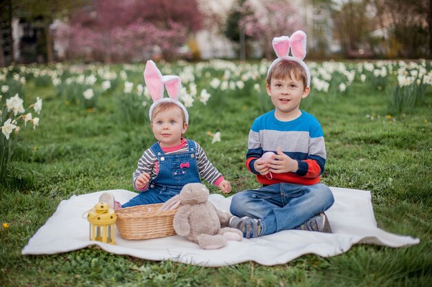 Little cute boy and girl are sitting on the grass near the daffodils