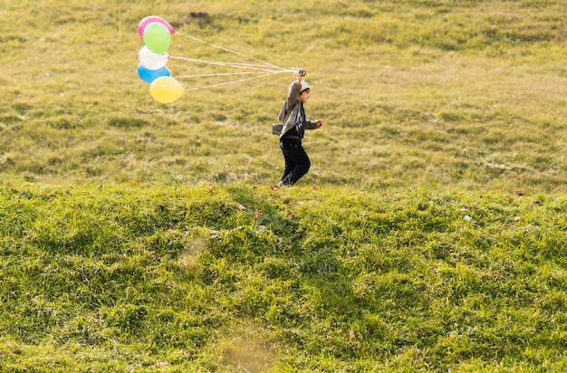 Little cute boy on grass meadow with balloons