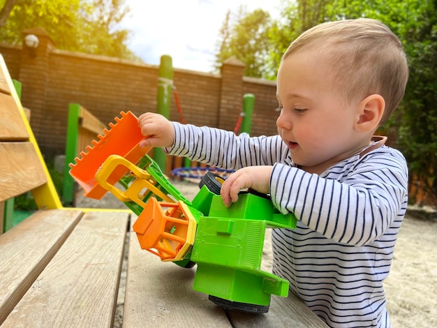 Маленький симпатичный мальчик полутора лет играет с игрушечной машинкой на детской площадке Очаровательный малыш, играющий с машинками и игрушками на открытом воздухе Концепция семейного отдыха и детского образа жизни Избирательный фокус