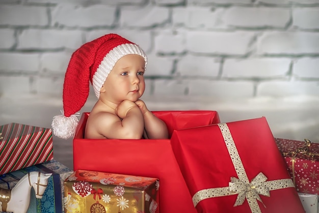 Little cute boy in a Santa hat sits in a gift box Christmas concept