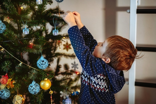 Little cute caucasian boy decorating Christmas tree with twinkling decorations