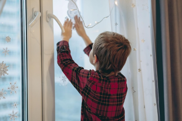 Photo little cute caucasian boy decorating window with christmas stickers