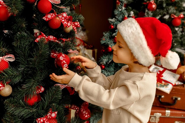 Little cute Caucasian boy helps to decorate the Christmas tree smiling in good expectation