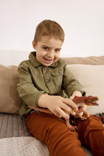 Foto un piccolo e carino ragazzo caucasico che gioca con i dinosauri a casa