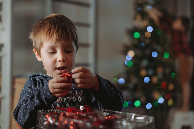 Little cute caucasian boys decorating Christmas tree with twinkling decorations