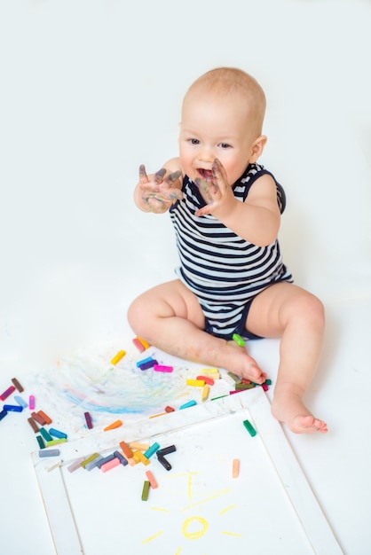 Little cute child with creativity draws with crayons at home on a sheet of white paper