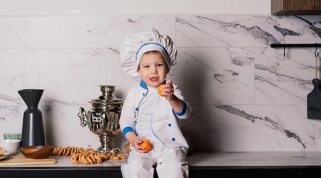 Little cute cook with cutlery sitting on a kitchen, twin brothers, tangerine, bagels