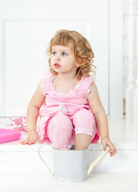 Little cute curly girl in a pink dress with polka dots sitting on the white porch Provence style