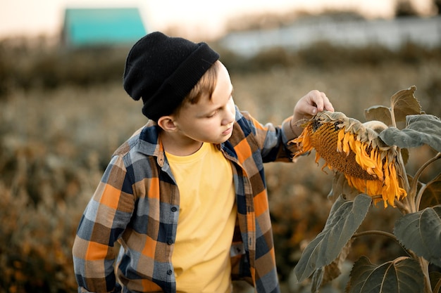 Foto il piccolo ragazzo sveglio dell'agricoltore vede il girasole è maturato in un giardino