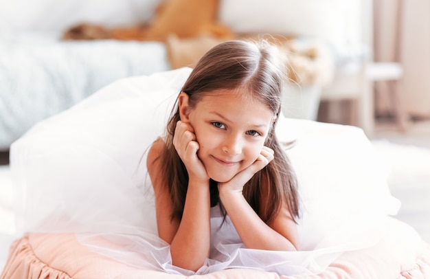 Little cute girl in a beautiful white dress resting in a light children's bedroom