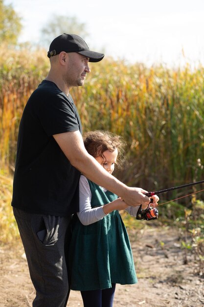 Foto piccola ragazza carina che cattura un pesce con papà nel lago, nel fiume o nello stagno