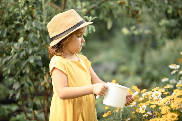 Little cute girl child with water can watering flowers in a garden backyard Kids gardening Outdoors children activity