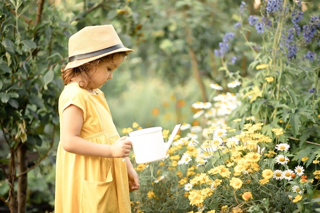 Little cute girl child with water can watering flowers in a garden backyard Kids gardening Outdoors children activity