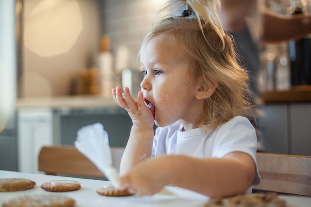 Little cute girl decorates gingerbread with sugar icing preparation for christmas concept