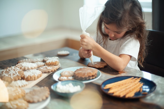 Little cute girl decorates gingerbread with sugar icing preparation for christmas concept