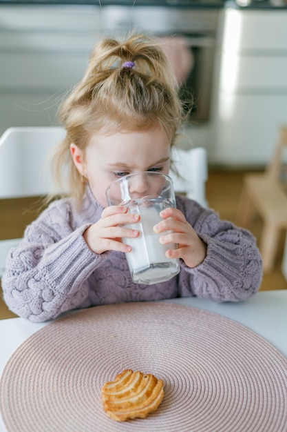 Photo little cute girl drinks milk and eats cookies. helthy.