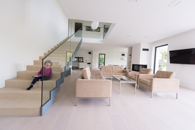 Little cute girl enjoying on the stairs in a modern living room\
of her luxury home