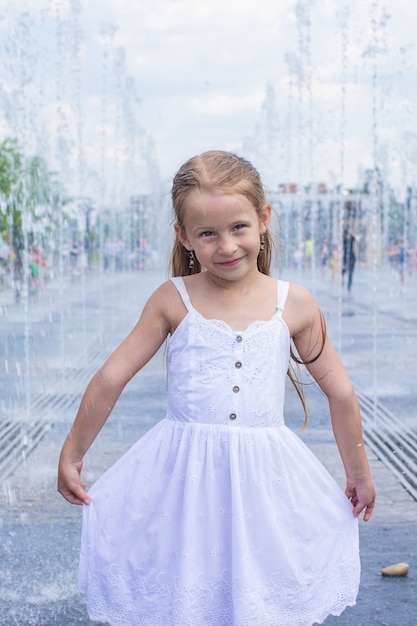 Little cute girl have fun in open street fountain at hot summer day