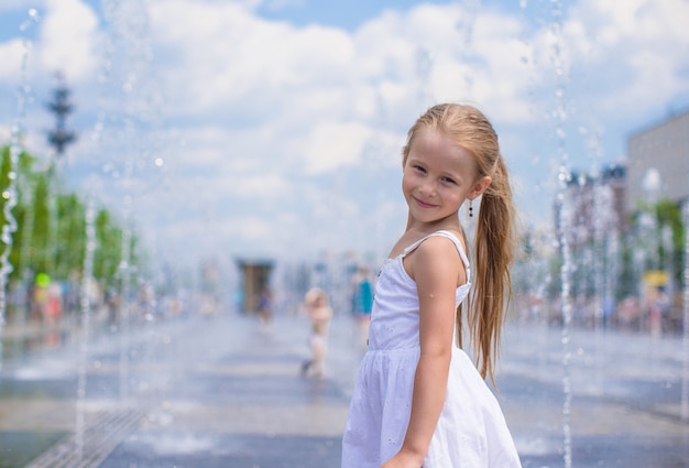 Little cute girl have fun in open street fountain at hot summer day