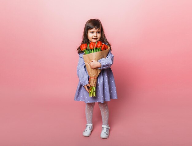 Little cute girl holding a bouquet of tulips in craft packaging on a pink background Happy womens day Place for text