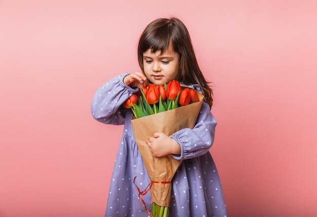 Little cute girl holding a bouquet of tulips in craft packaging on a pink background Happy womens day Place for text