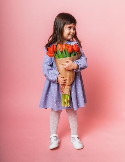 Little cute girl holding a bouquet of tulips in craft packaging on a pink background Happy womens day Place for text