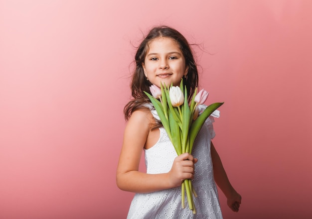 Little cute girl holding a bouquet of tulips on a pink background Happy womens day Place for text Vivid emotions March 8