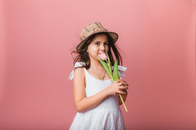 Little cute girl holding a bouquet of tulips on a pink background Happy womens day Place for text Vivid emotions March 8