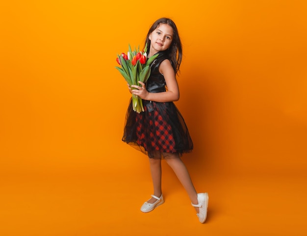 Little cute girl holding a bouquet of tulips on a yellow background Happy womens day Place for text Vivid emotions March 8