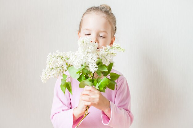 Photo little cute girl holding a bouquet of white lilac in her hands. admires, looks, gives to mother. mothers day