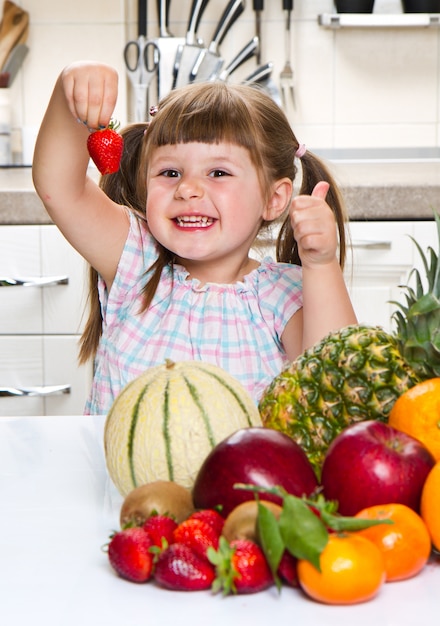 Little cute girl holding and eating a strawberry in the kitchen