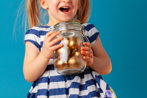 Little cute girl holding glass jar with golden eggs colored for Easter