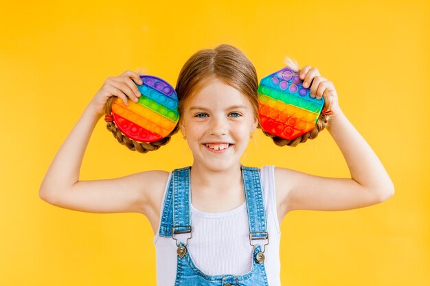 Little cute girl holding pop it antistress toy on yellow background, isolate. copyspace