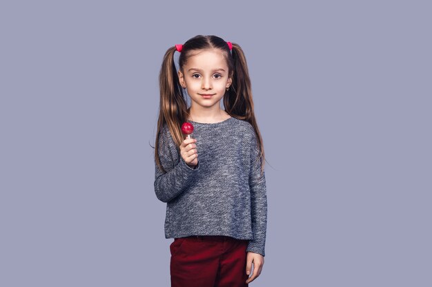 Little cute girl holding a red lollipop. isolated on gray background