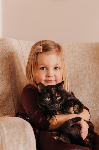 A little cute girl holds a black cat in her arms. Girl at home with her pet. Little girl loves her cute kitten.