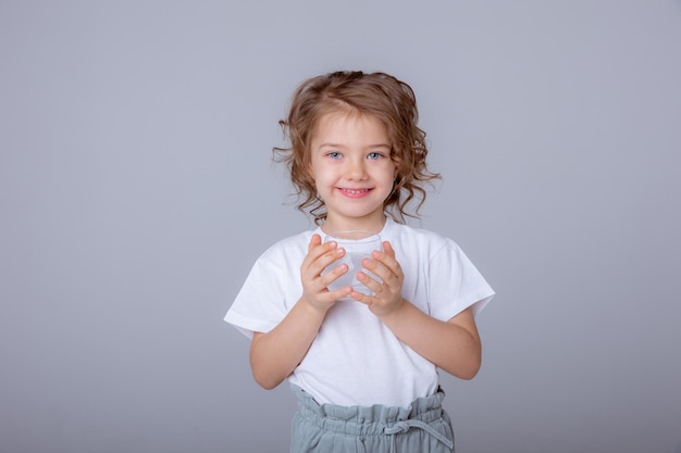 小さなかわいい女の子が水差しを持って白い背景で隔離のガラスに水を注ぐ