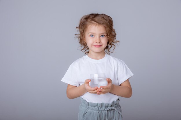 小さなかわいい女の子が水差しを持って白い背景で隔離のガラスに水を注ぐ