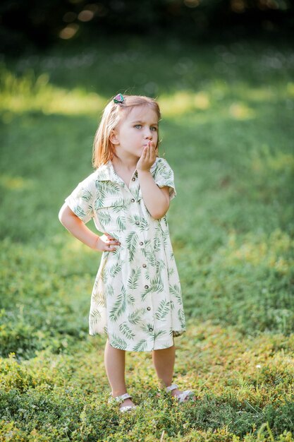 Little cute girl is sitting on the grass. Happy girl in the park. Summer.