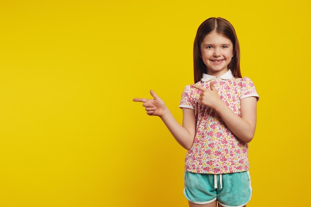 little cute girl kid points away with both forefingers shows blank space