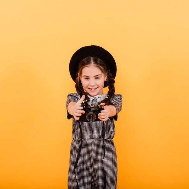 A little cute girl making photo on yellow background.