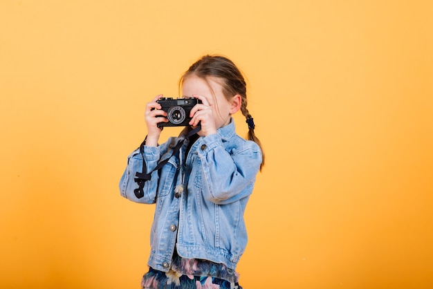 A little cute girl making photo on a yellow wall.