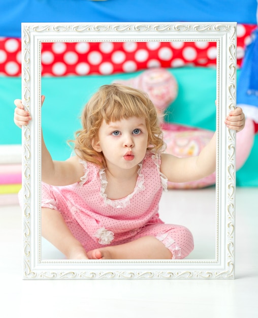 Little cute girl in a pink suit sitting on the floor and smiling over wooden white frame.